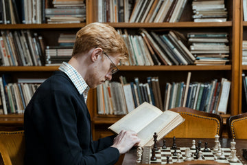 man reading a book next to a chess board
