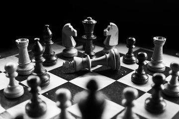 black and white chess pieces surrounding a fallen king piece