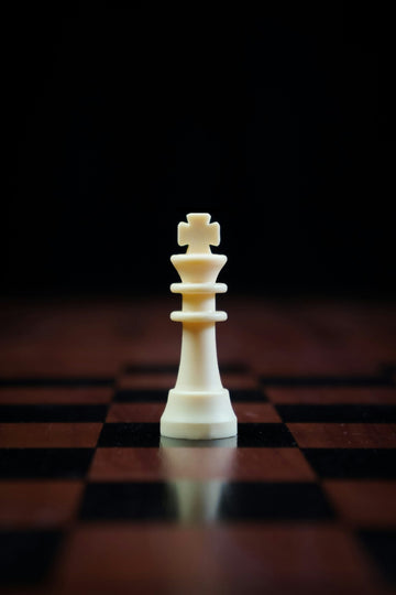 White king chess piece on the center of a chess board against a black background.